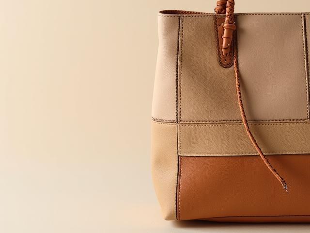 Gros plan d'un sac à main upcyclé sophistiqué, fait à partir de chutes de cuir beige et camel, montrant des coutures fines et détaillées.